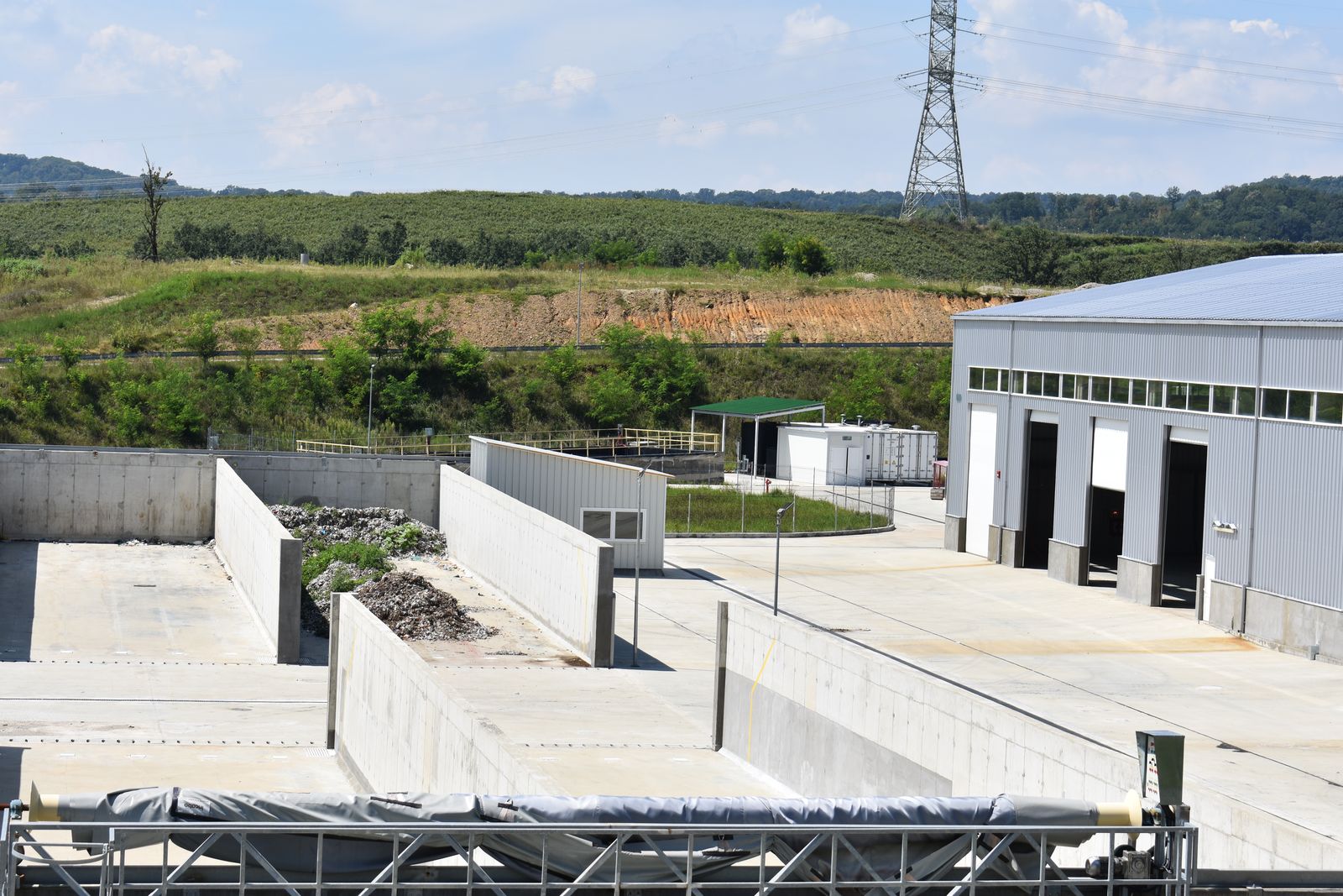 Hală industrială și platforme de beton ale stației de sortare, cu dealuri în fundal